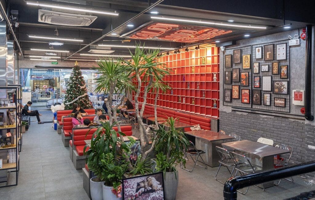 Không gian bên trong Kaldi And More Danang với sofa đỏ, bàn kim loại và cây xanh bố trí dọc lối đi