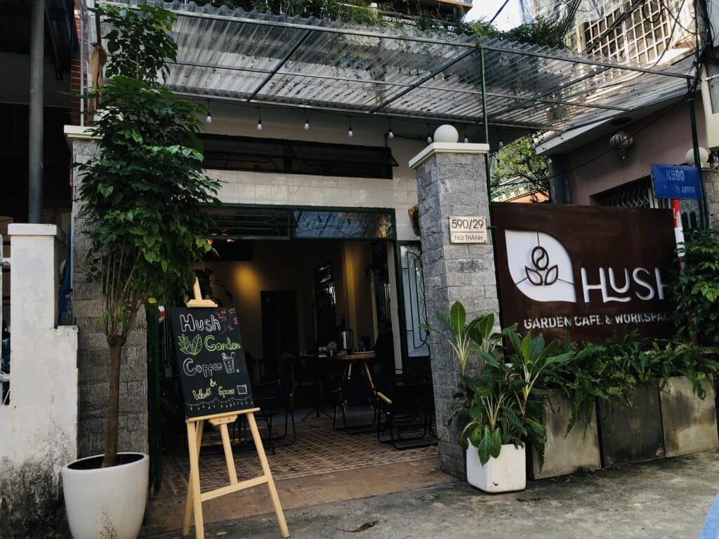 Mặt tiền Hush Garden Cafe & Workspace với lối vào phủ nhiều cây xanh và bảng hiệu quán