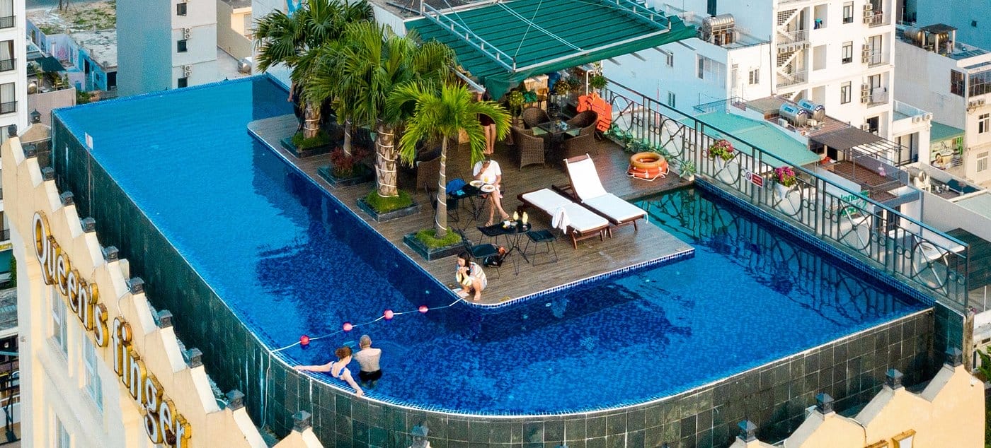 Hồ bơi vô cực trên sân thượng Sea Queen Hotel với ghế nằm, cây xanh và khung cảnh thành phố